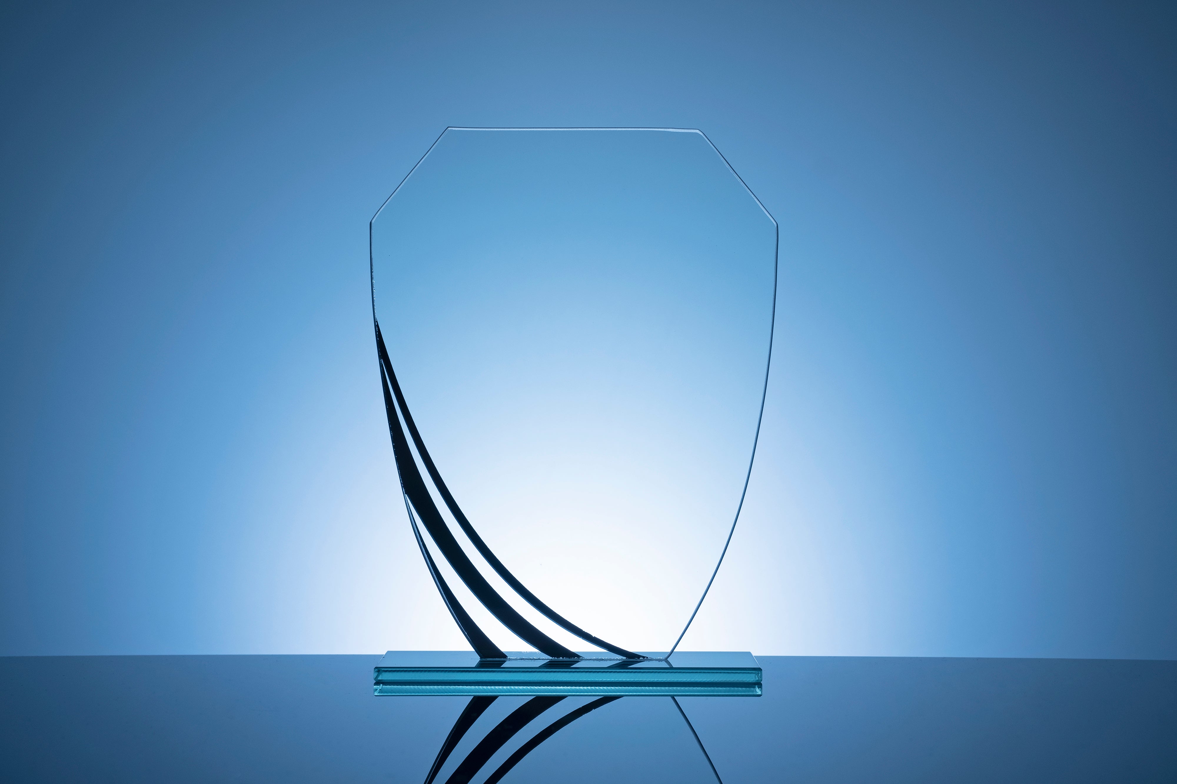 Unique award ideas: Modern crystal shield trophy with elegant curved black accents on glass base, backlit against blue background.